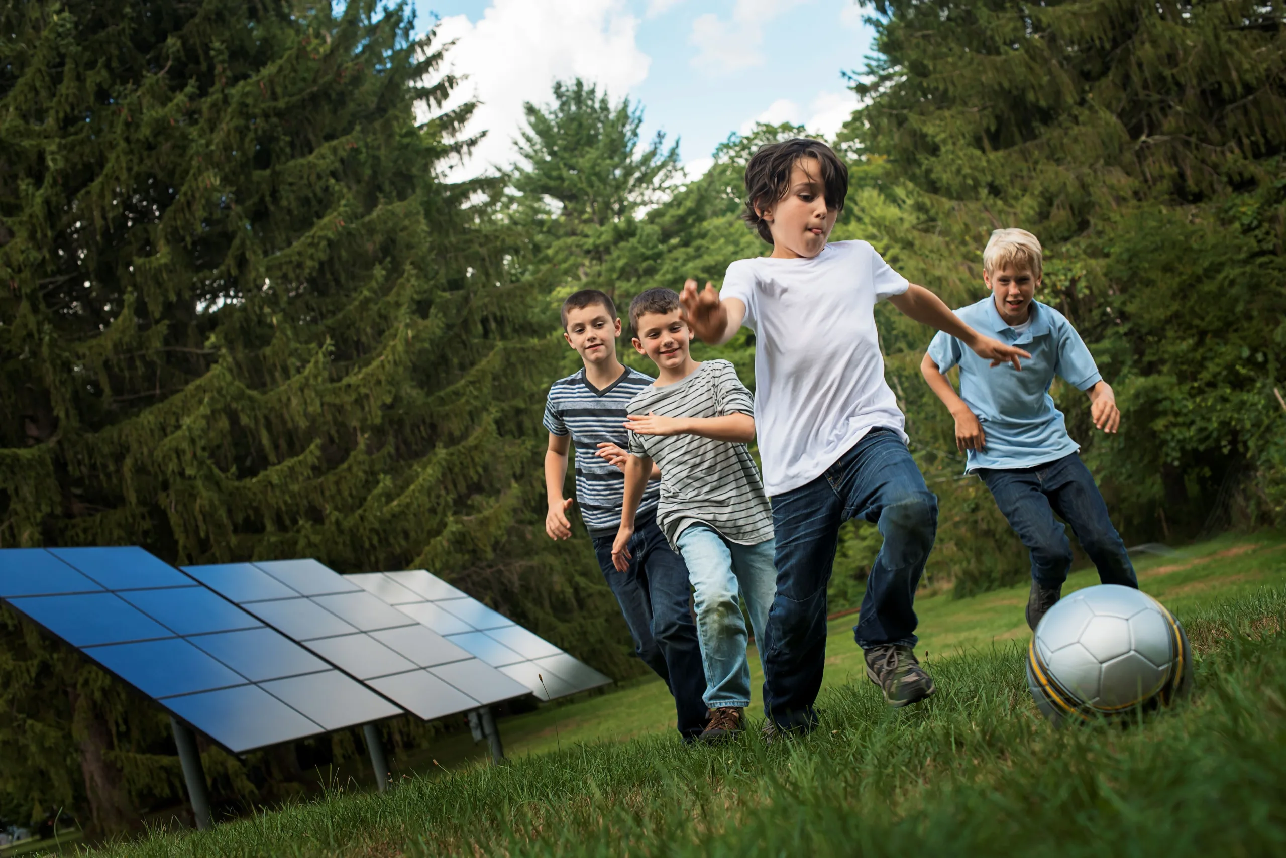 Un grupo de chicos corriendo detrás de una pelota pasando por paneles solares en el bosque.